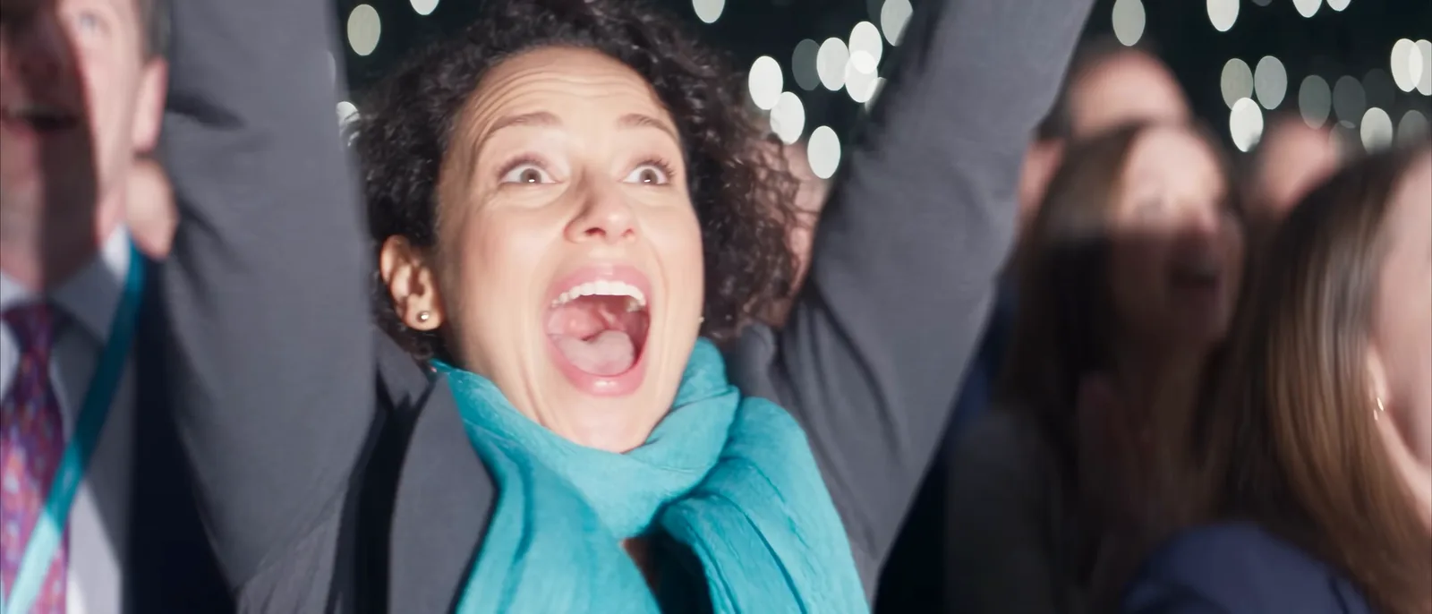 A woman in the crowd throws her arms up and shouts with joy