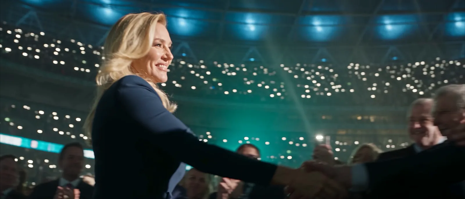 Brooke shakes hands with the crowd, the lit arena behind her